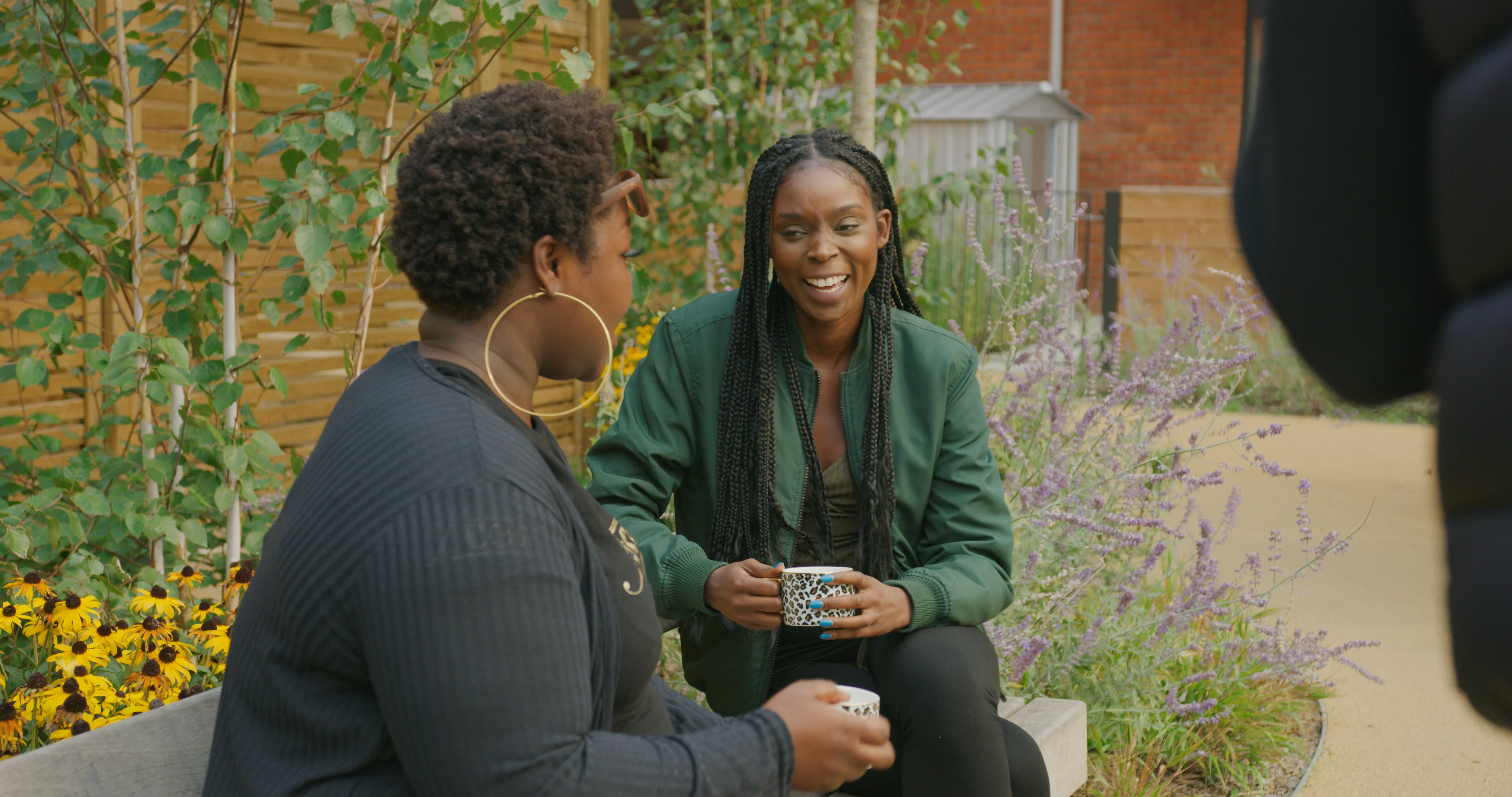 Two women sat on a bench outside are chatting