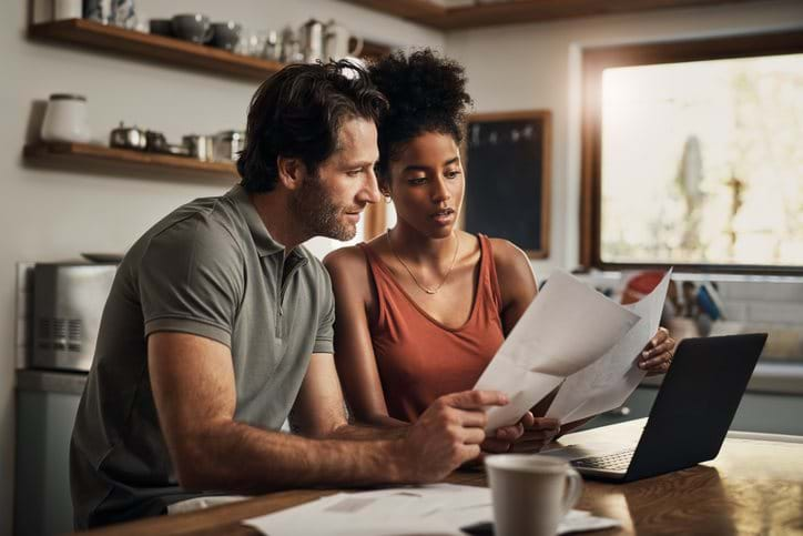 Couple assessing finances, looking at bills and computer