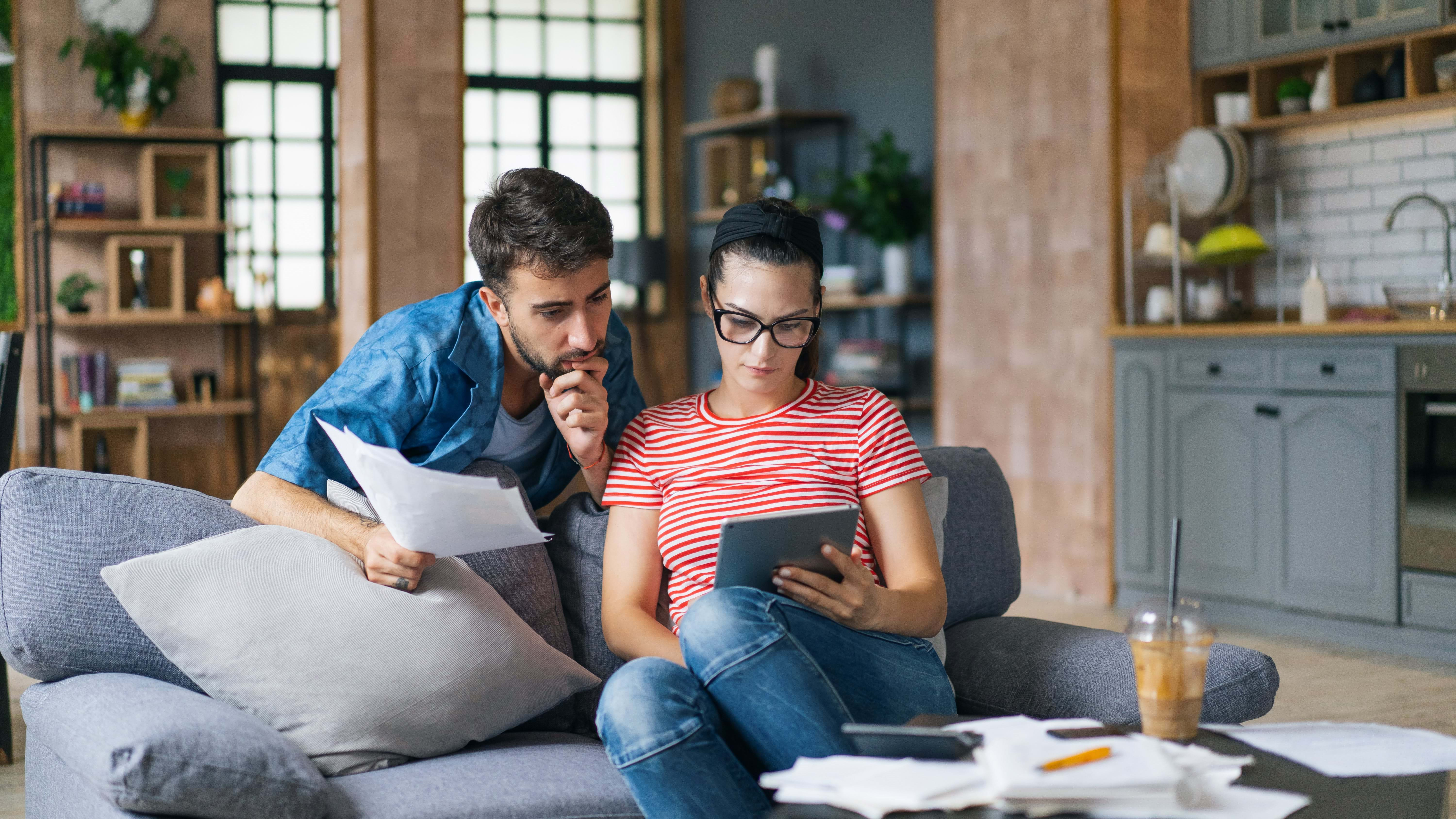 Couple sat on sofa looking at tablet and bills