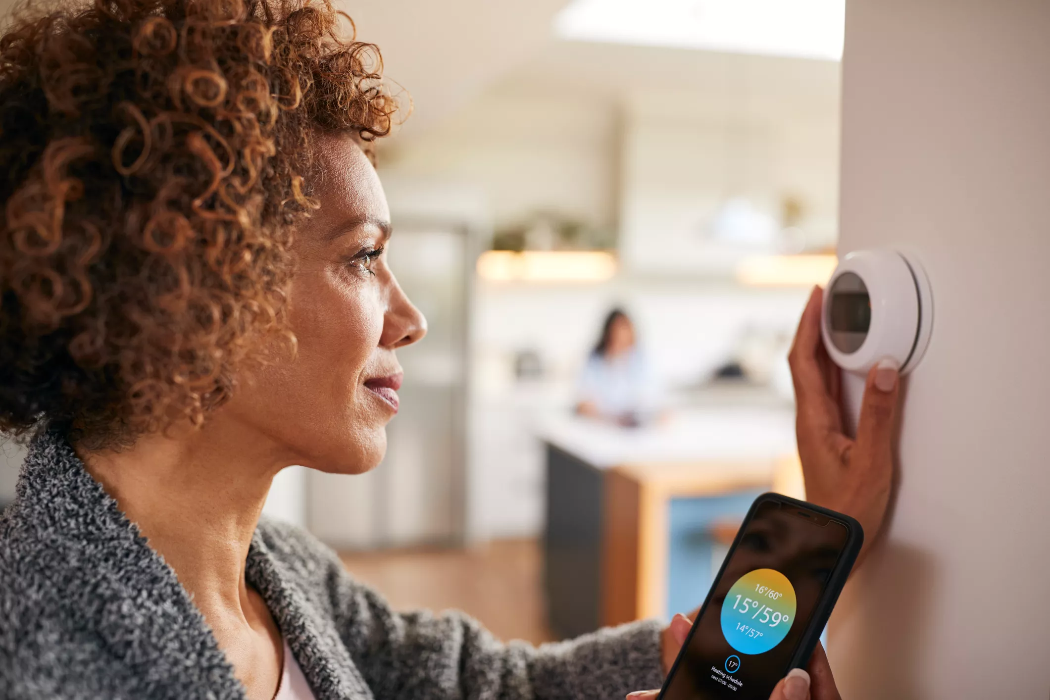 Woman adjusting her central heating thermostat using her phone